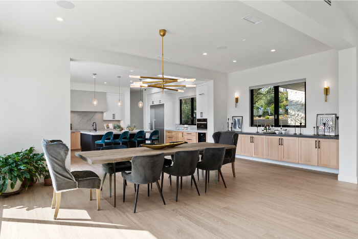 Open dining room and kitchen with long wood table, upholstered chairs, modern lighting, and light wood cabinetry.